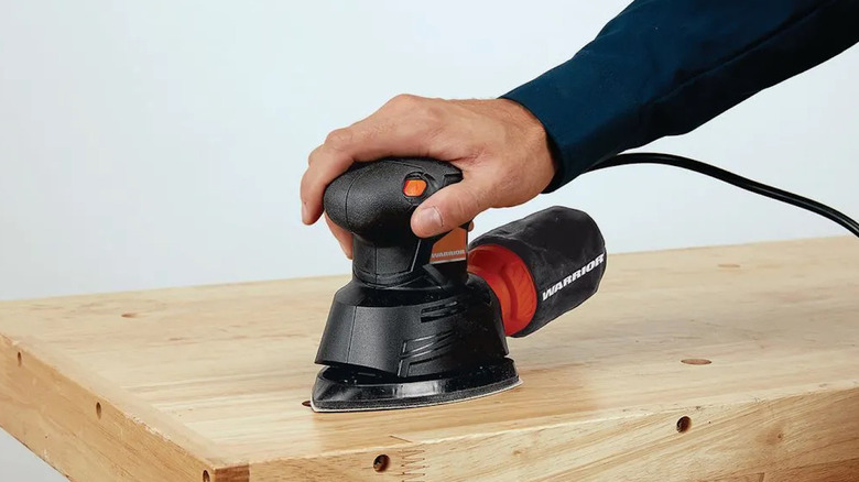 Hand holding Harbor Freight's Warrior Corner/Detail Sander on wooden workbench