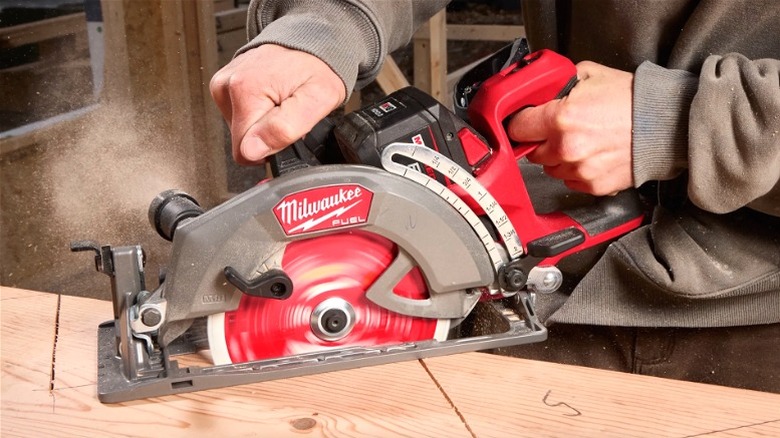 Person cutting through wood board with Milwaukee rear-handle circular saw.