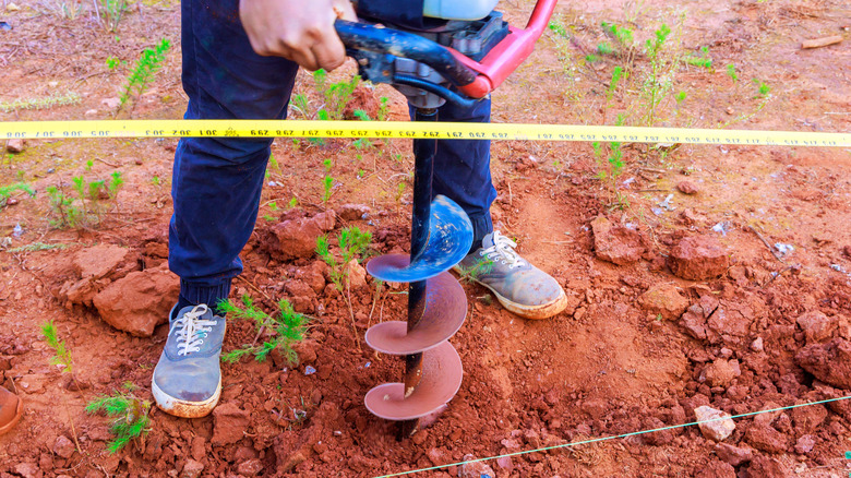 A man using an auger to drill a post hole