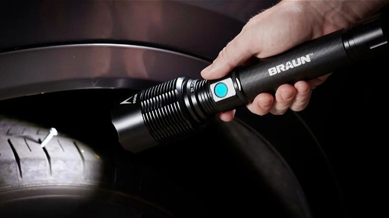 Hand holding a Braun flashlight to illuminate a nail stuck in a rubber tire.