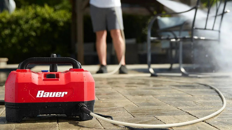 Bauer power washer on top of patio pavers with a man washing furniture in the background.