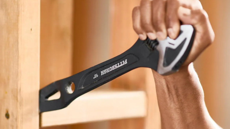 A person using the multipurpose pry bar wrench on a wood plank.