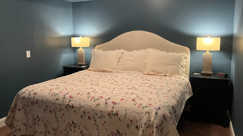 A basement bedroom with blue walls and a floral bedspread