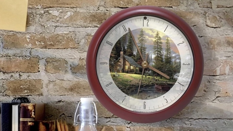 A Thomas Kinkade Peaceful Retreat Meditative Nature Sound Clock on a brick wall above a shelf