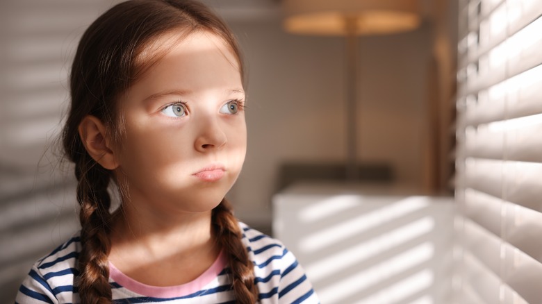 Sun shines through a window blind onto a young girls face