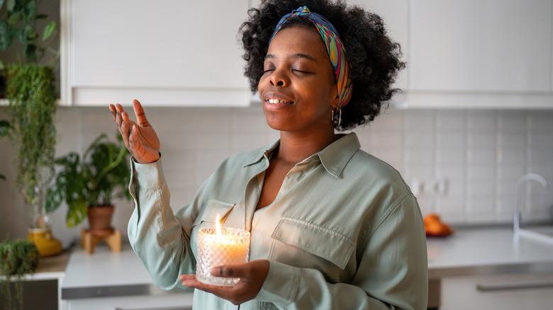 A person enjoying the scent of a lit candle she is holding
