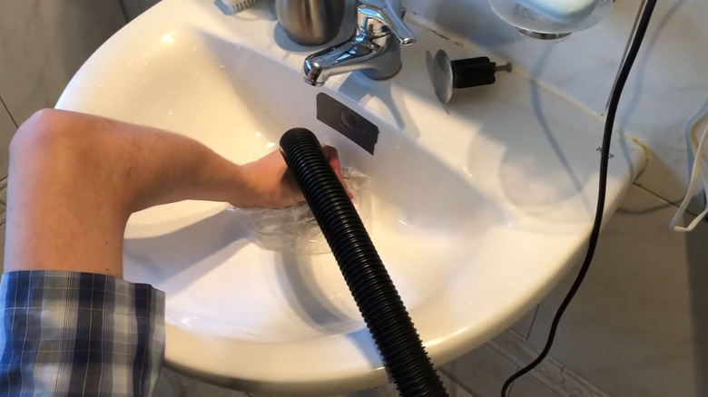 Someone unclogging a drain using a shop vac