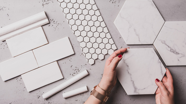Hands holding a hexagonal tile with other tile options laying on a flat surface.