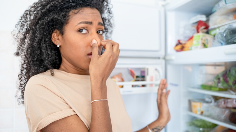 Woman holding nose by fridge