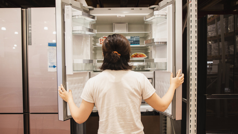 A woman in a white tee shirt opening a double-door refrigerator at a store