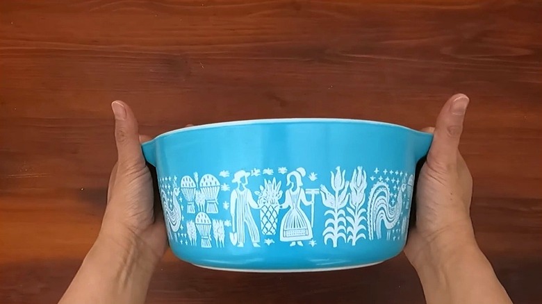 A person holds a vintage blue and white Pyrex casserole in the pattern known as Amish Butterprint.