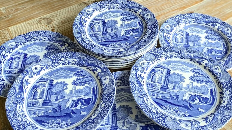 A collection of Spode dishware in the white and blue Blue Italian pattern showing scenes of rural life in the center and adorned with flower and plant designs on the borders.