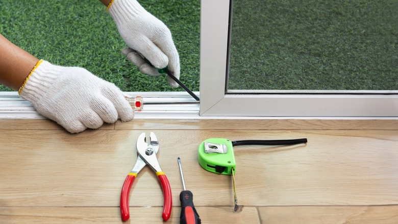 A person adjusting screws on a sliding glass door