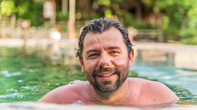 A man smiling at the camera while wet and in a pool