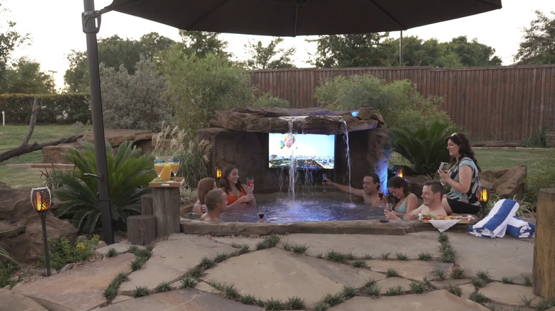 a faux-stone hot tub with a waterfall and outdoor television