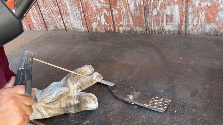 Man welding a handle onto an old lawn mower blade to make wire cutters