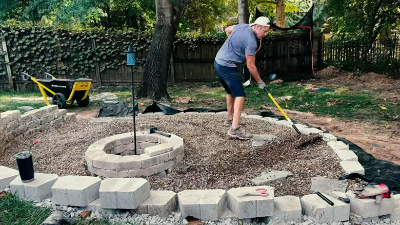 A person using a rake to spread out gravel in a patio between two retaining walls