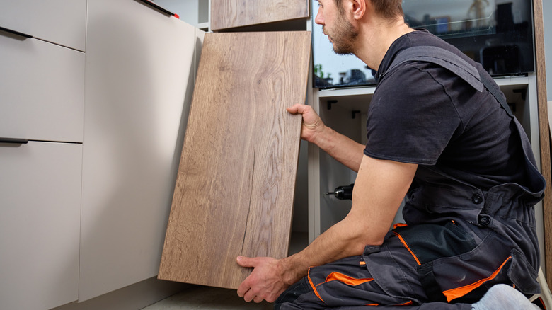 A guy holds wood close to gray kitchen cabinets before a makeover
