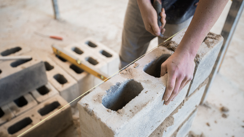 A person assembles cinder blocks into a wall.