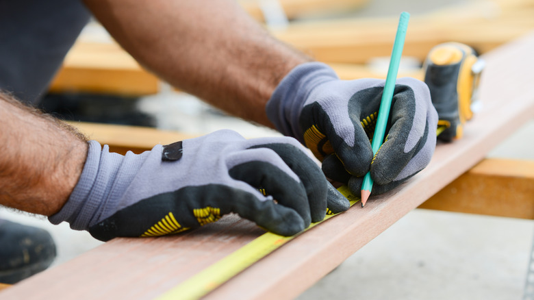 Person in protective gloves measuring wood before cutting it