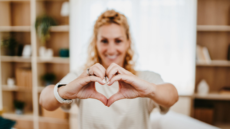 Smiling young woman making a heart sign with her hands and bustling street activity in the background