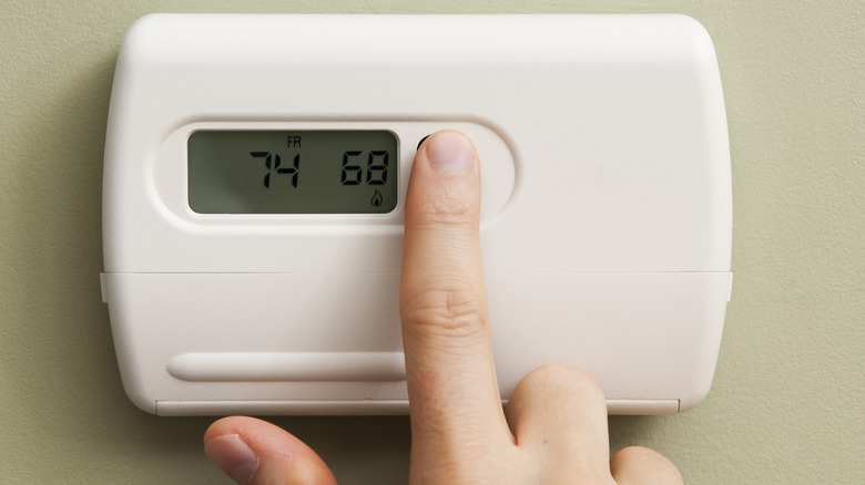 Person adjusting the setting on a thermostat