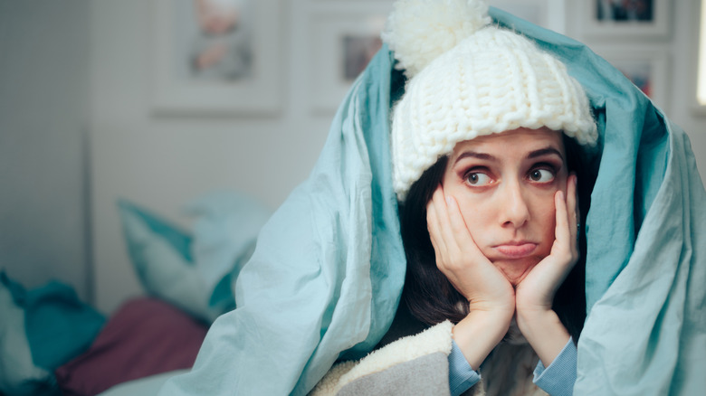 Woman bundled up and under covers in bed because it's cold in her bedroom.
