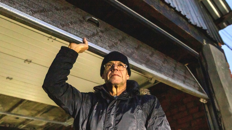 Older man in winter coat and hat lifting garage door