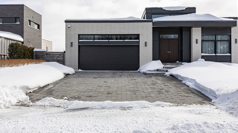 Driveway cleared of snow leading to garage and house beside snowy yard.