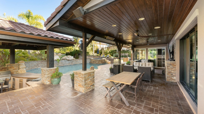 A luxury outdoor living space with covered patio, pool, lush landscaping, and stone accents.