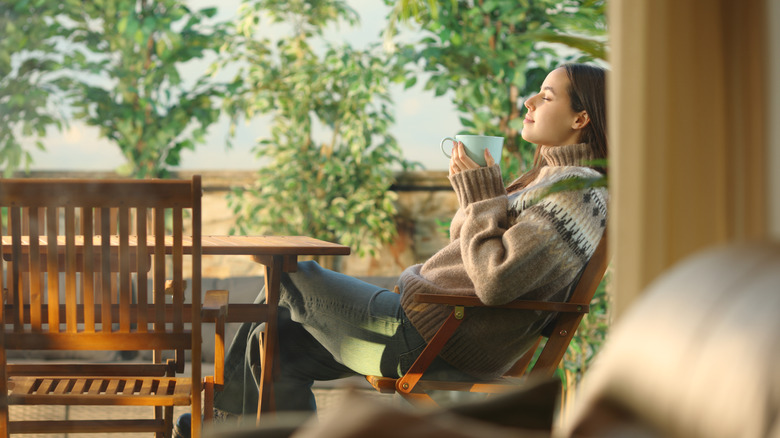 Woman sitting outdoors on a patio drinking coffee.