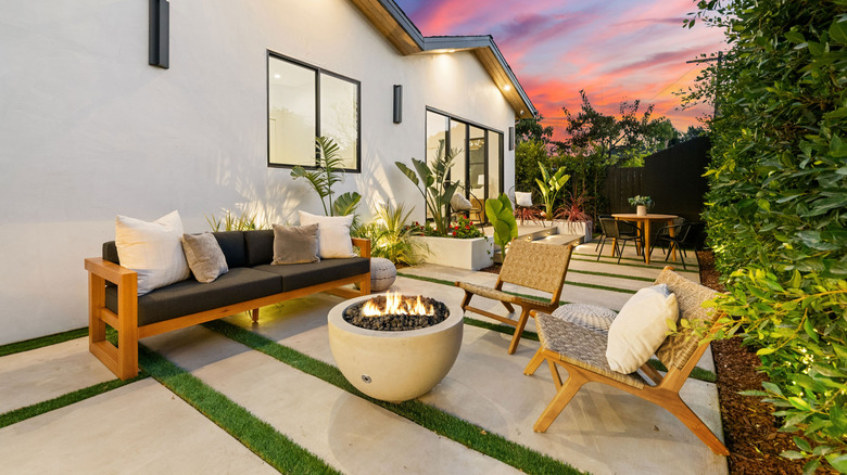 Modern outdoor patio with cozy seating and fire pit, set against a vibrant sunset sky, showcasing contemporary design and lush greenery.