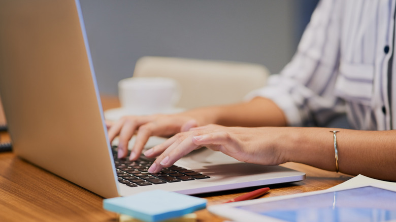 Hands typing at a laptop, a person using their computer for research