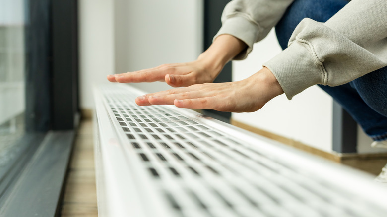 A person's hands feel for heat coming off of a radiator