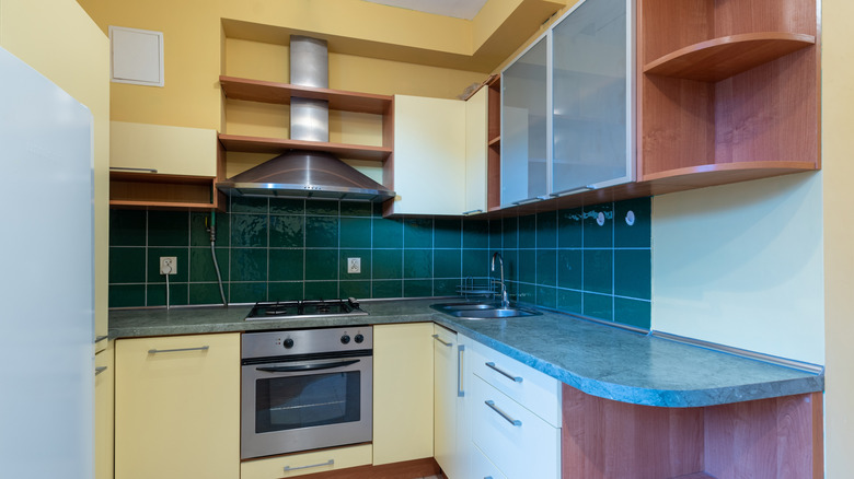 Classic old style kitchen interior with green backsplash, yellow and white cabinets, and brown shelving