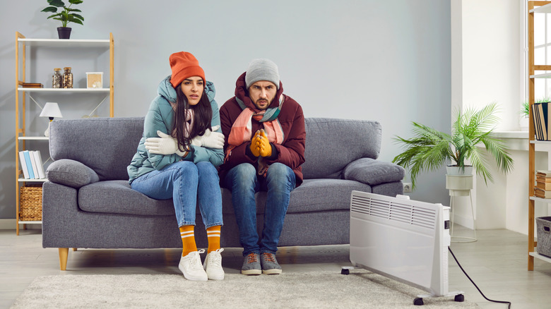 A man and woman are bundled up inside their cold living room.