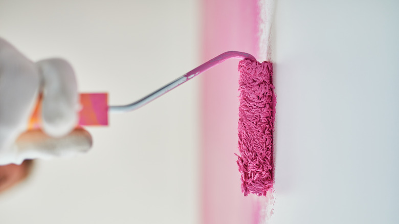A closeup of a hand painting a wall in pink using a paint roller