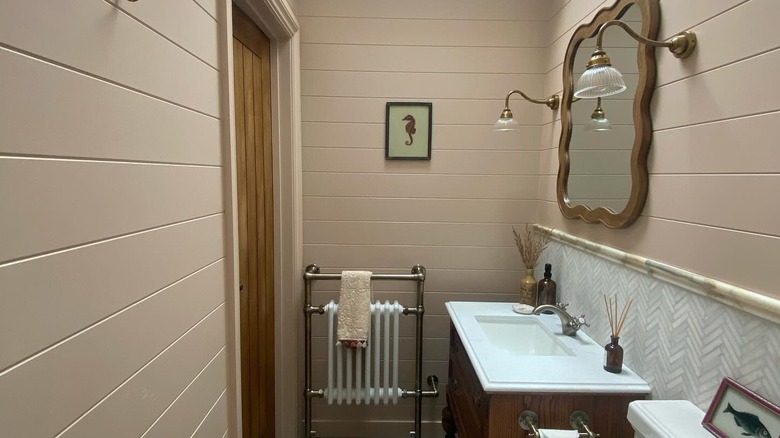 A vintage style bathroom with paneled walls painted in blush pink