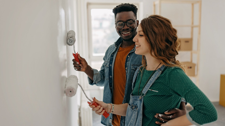 Young couple painting walls with paint rollers together