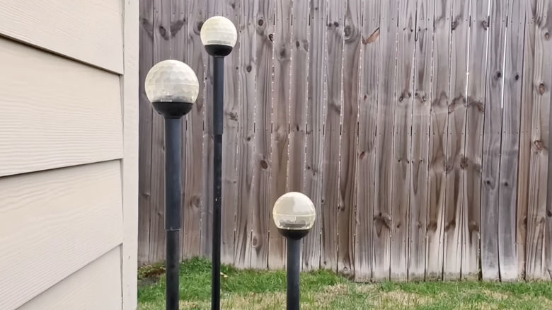 Three Dollar Tree solar lights on dowels in a backyard.