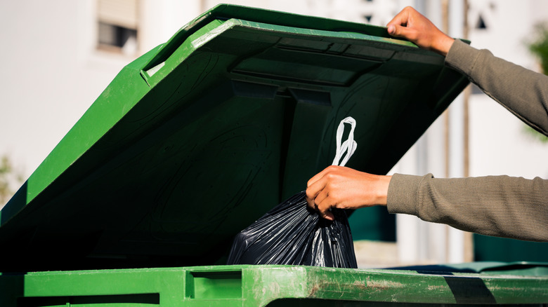 Person placing a trash bag in the main garbage can outdoors