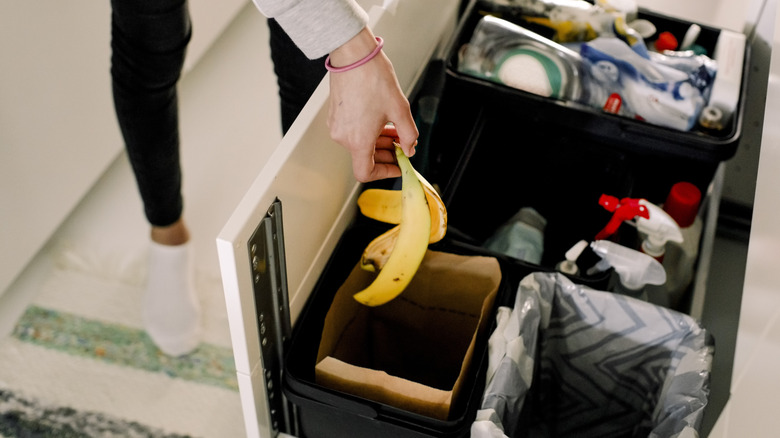 Person dropping banana peel into indoor trash can