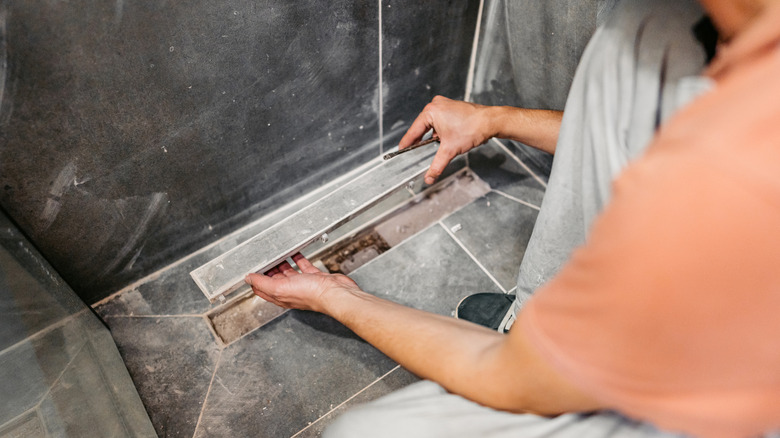 A person installing a shower drain.