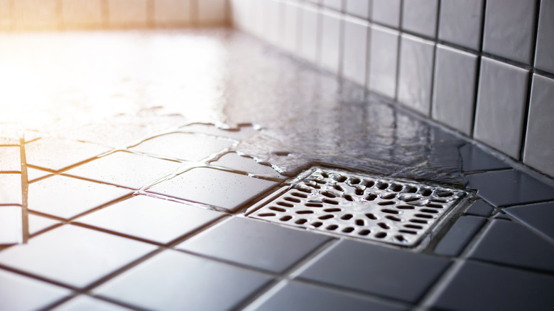 Water flowing over a tiled floor into a shower drain.
