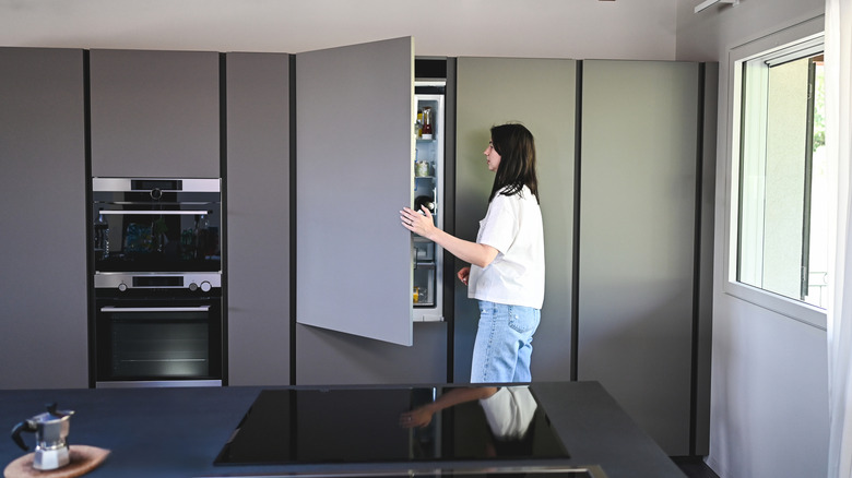 Woman opening panel ready refrigerator in modern kitchen