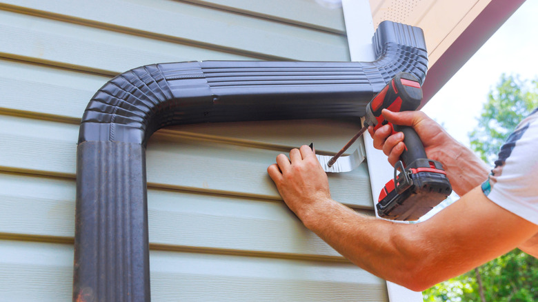 A person uses a drill to install a rain gutter.