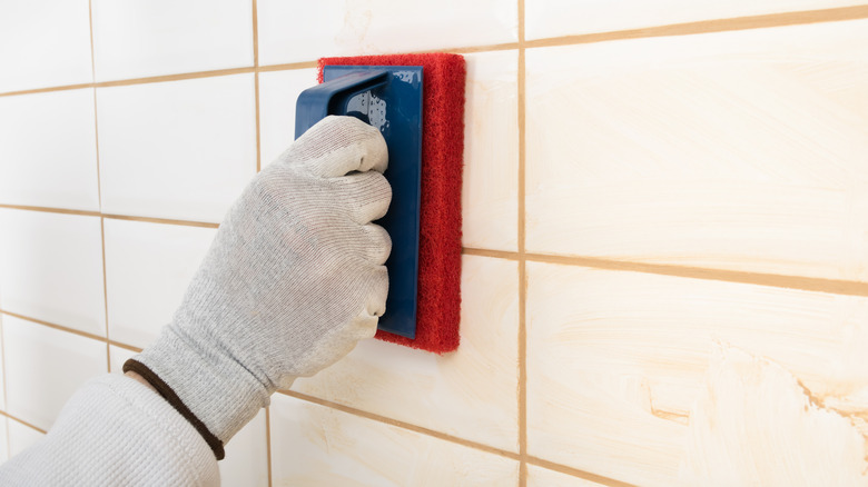 Rubbing grout on white shower tiles.