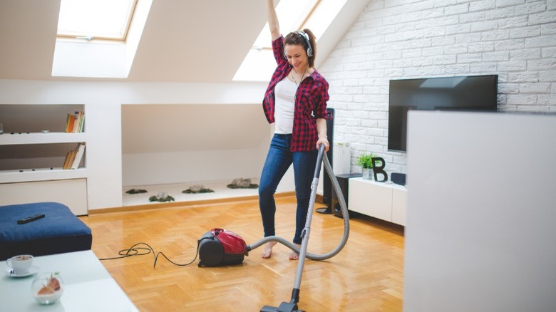 Happy woman vacuuming wood floor 