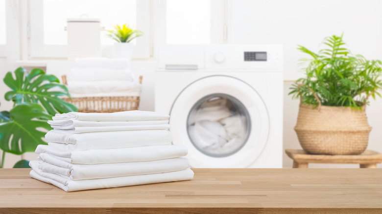 Freshly-washed white bed sheets sit on a wood counter in the laundry room