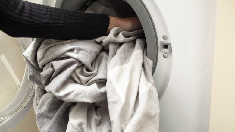 A person loads light gray sheets into a washing machine